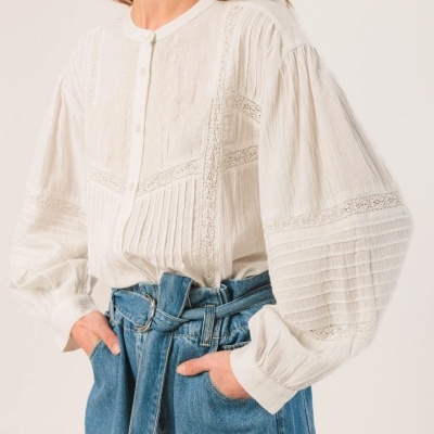 Blusa branca com mangas bufantes e detalhes em renda usada com calças jeans azuis.