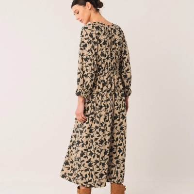 Mulher vista de costas usando vestido comprido floral bege e preto com botas castanhas