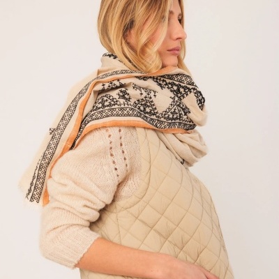 Pessoa de perfil com colete acolchoado bege e lenço padrão preto com borda laranja