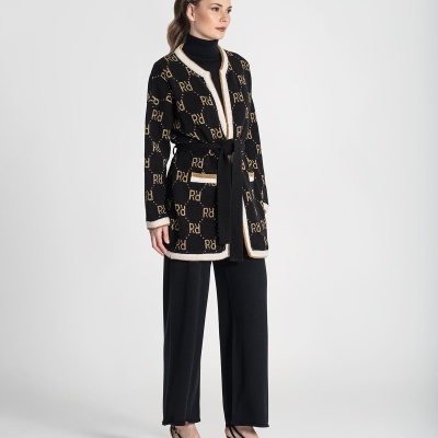 Mulher vestindo casaco preto com padrão 'Rd' bege, camisola gola alta preta, calças largas pretas e sapatos de salto pretos.