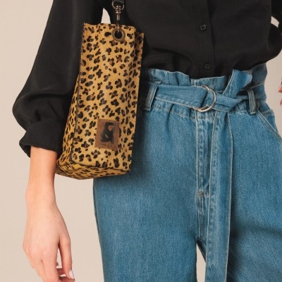 Bolsa pequena com padrão animal print bege e preto com alça preta e patch castanho, usada com camisa preta e calças de ganga azuis.