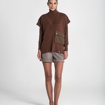 Mulher com colete castanho de malha e calções cinza em fundo branco