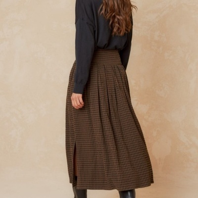 Mulher a usar camisola preta e saia comprida xadrez castanho e preto com botas pretas.