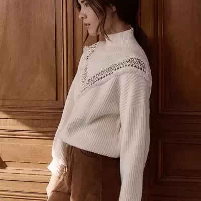 Mulher com camisola branca de malha e calções castanhos de camurça, com collants pretos