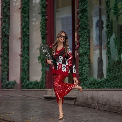 Mulher com casaco de estrelas, saia vermelha de lantejoulas e óculos de sol numa rua com guirlandas verdes.