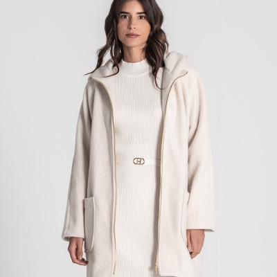 Mulher com casaco bege claro e vestido branco canelado com cinto