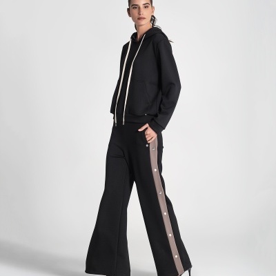 Mulher com hoodie preto e calças pretas flare com faixa castanha e botões laterais.