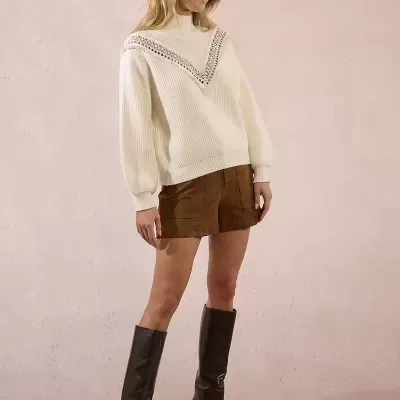 Mulher com camisola branca de gola alta, saia castanha e botas pretas altas