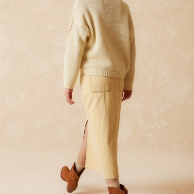 Mulher veste gorro vermelho, camisola creme, saia bege longa e botins castanhos