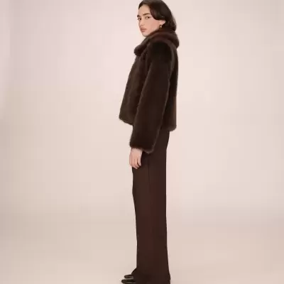 Mulher com casaco de pele castanho escuro, calças castanho escuro e sapatos pretos em fundo claro