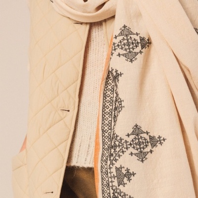 Echarpe bege claro com bordado preto geométrico sobre casaco acolchoado bege e camiseta tricotada branca