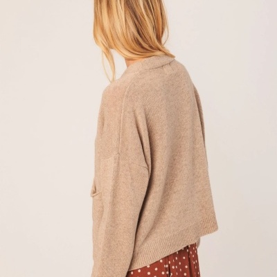 Mulher de costas com camisola castanha clara de malha e saia castanha às bolinhas brancas.