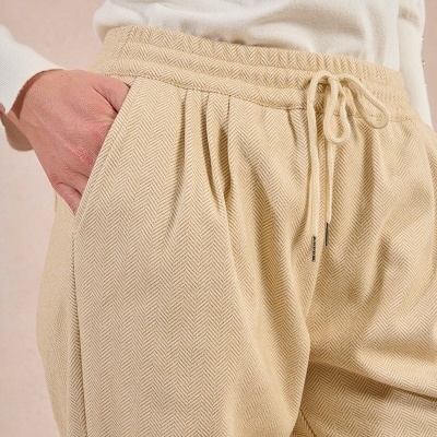 Calças bege com padrão espinha de peixe e cordões na cintura, usadas com camisa branca.