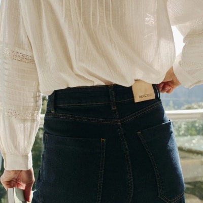 Calças de ganga azul escuro com camisa branca de renda, vista das costas junto a uma varanda