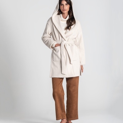 Mulher com casaco bege com capuz e cinto, camisola branca, calças castanhas e sapatos castanhos