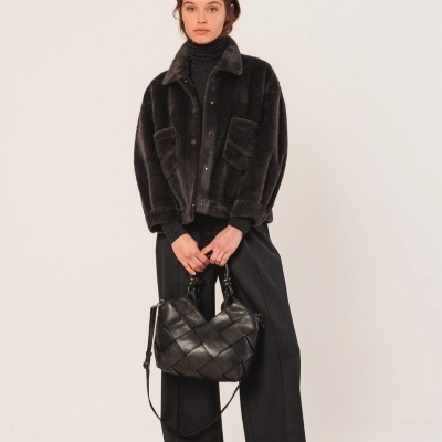 Mulher vestindo casaco de pelo preto, calças pretas e segurando bolsa de couro preta