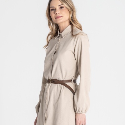 Mulher com vestido bege e cinto castanho, em fundo branco.