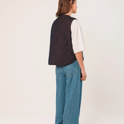 Mulher de costas com colete xadrez, t-shirt branca e calças de ganga azuis