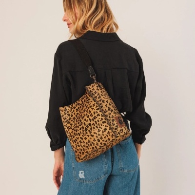 Mochila padrão leopardo alça preta usada por mulher com camisa preta e calças azuis de ganga