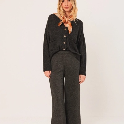 Mulher vestindo conjunto de malha preta com botões e calças largas, lenço no pescoço e sapatilhas castanhas com padrão