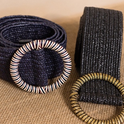 Dois cintos trançados azul e preto com fivelas redondas decoradas, sobre tecido castanho.