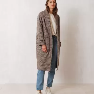 Mulher com casaco comprido pied-de-poule, camisola branca, calças de ganga e ténis brancos