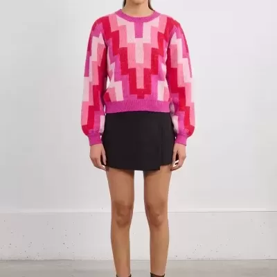 Mulher a usar camisola com padrão geométrico rosa e vermelho e saia preta curta