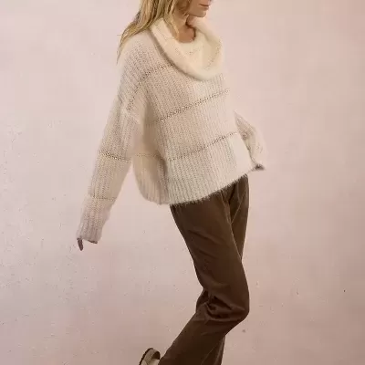 Mulher com sweater de malha creme, calças castanhas e sapatos bege
