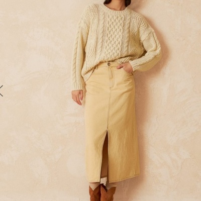 Mulher com camisola de malha creme, saia midi bege, botas castanhas e gorro vermelho