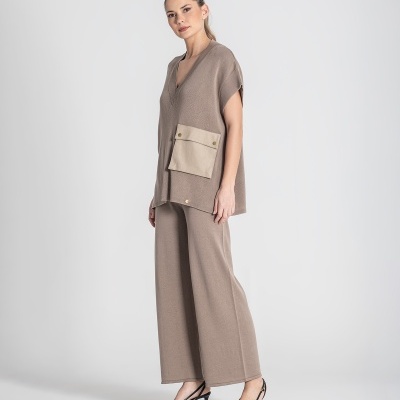 Modelo feminina com conjunto bege de blusa e calças largas e sapatos pretos de salto.