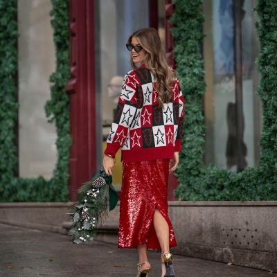Mulher com camisola de estrelas e saia vermelha de paetês, a andar numa rua com decoração verde natalícia