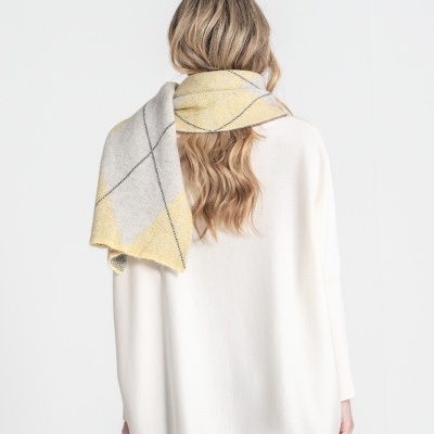 Cachecol xadrez em cinza, amarelo e bege, atrás de uma pessoa com camisola branca e calças de ganga.