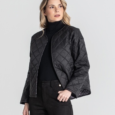 Casaco acolchoado preto com padrão de losangos, usado com roupa preta sobre fundo cinzento claro