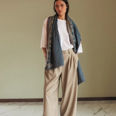 Mulher com t-shirt branca, calças bege e lenço azul com bordados