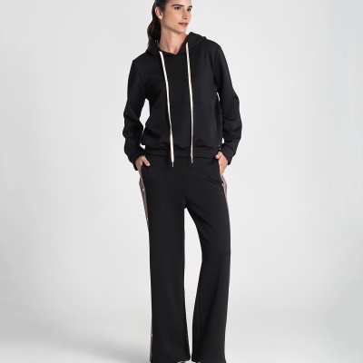 Mulher vestindo conjunto desportivo preto com hoodie e calças largas em fundo branco.