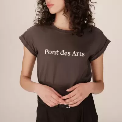 Mulher a usar t-shirt castanha escura com a frase Pont des Arts em branco na frente