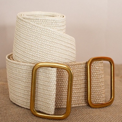 Cinto tecido bege com fivela dourada sobre superfície castanha