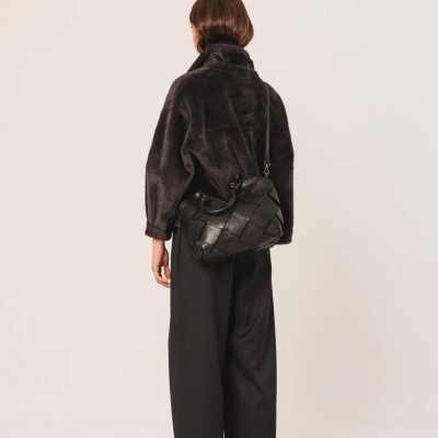 Mulher de costas com casaco peludo preto, calças largas pretas e bolsa de couro preta entrelaçada.