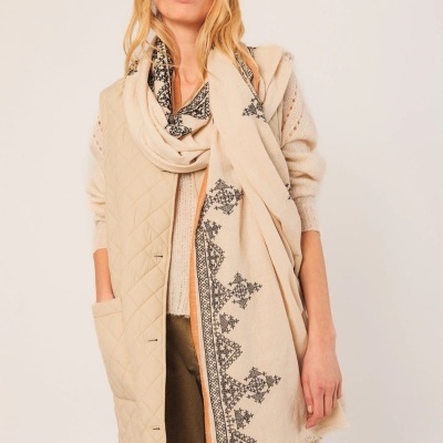 Mulher com echarpe bege com padrão geométrico preto, casaco acolchoado bege e blusão bege