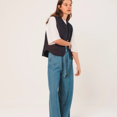 Mulher com colete xadrez azul escuro e vermelho, camiseta branca e calças de ganga largas azuis claras