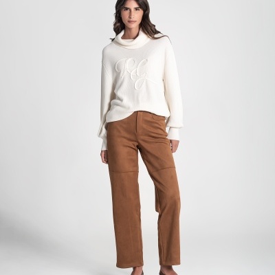 Mulher com calças castanhas e blusão branco com letras RG em relevo.