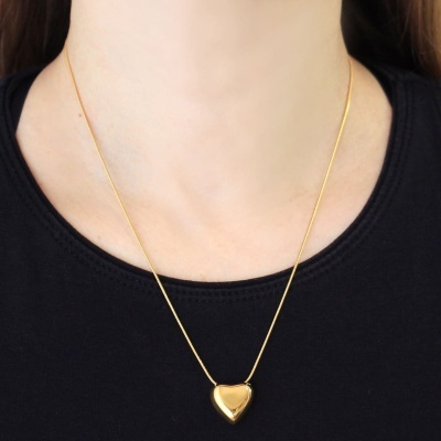 Colar dourado com pendente em coração sobre camiseta preta.