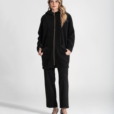 Mulher com casaco preto felpudo comprido com capuz e fecho dourado, calças pretas e sapatos de salto preto