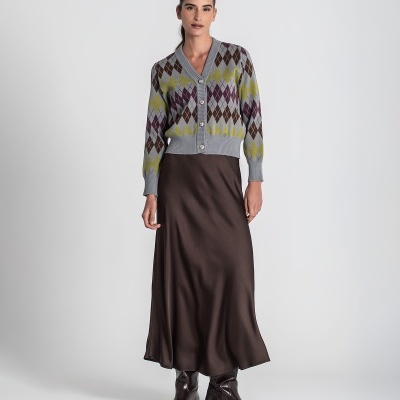 Mulher com camisola cardigan de losangos e saia comprida castanha em fundo cinza.
