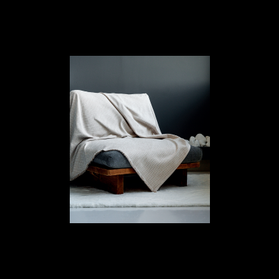 Cama baixa com manta bege clara sobre colchão cinza numa sala com parede cinza escuro e tapete branco