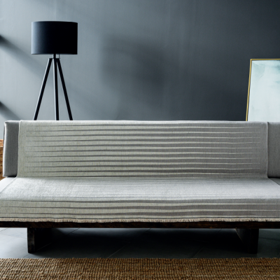 Sofá-cama cinzento numa sala moderna com candeeiro de pé, cesta de vime e quadro