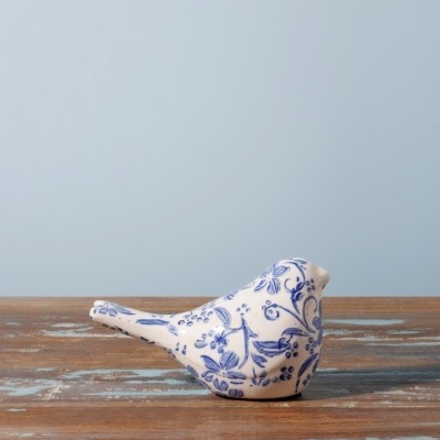 Escultura de cerâmica branca com padrões florais azuis em forma de pássaro sobre madeira rústica