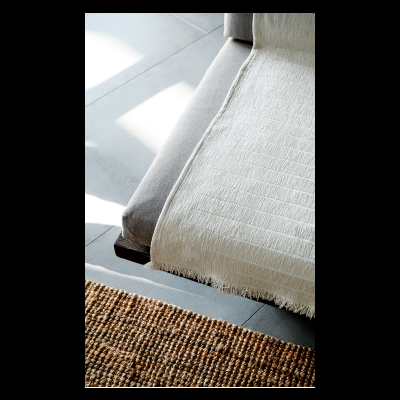 Sofá cinza claro com manta branca texturada e tapete castanho de fibras naturais