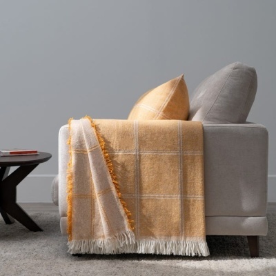 Sofá cinzento claro com almofadas e manta xadrez amarelo e bege com franjas