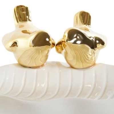 Estatuetas de pássaros dourados sobre base branca com padrão de folhas.